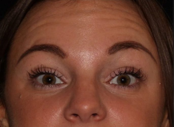 Close-up of a woman's face focusing on her eyes, showing light brown irises, neatly shaped eyebrows, and long lashes, with a neutral facial expression.