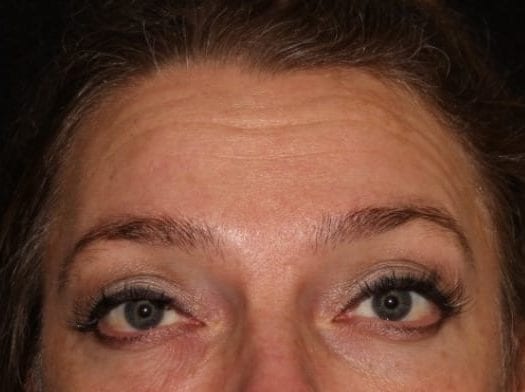 Close-up of a woman's eyes looking directly at the camera, showcasing detailed eye makeup and long eyelashes. her eyebrows are slightly raised, and the skin shows natural textures.