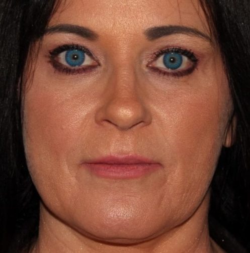 Close-up portrait of a woman with striking blue eyes, dark hair, and fair skin, looking directly at the camera.