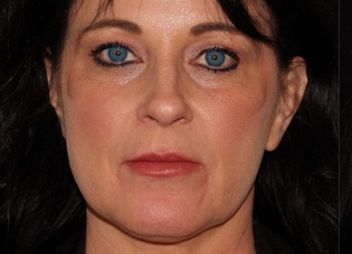 Close-up of a woman with bright blue eyes, fair skin, and dark hair. she is wearing subtle makeup and has a neutral expression.