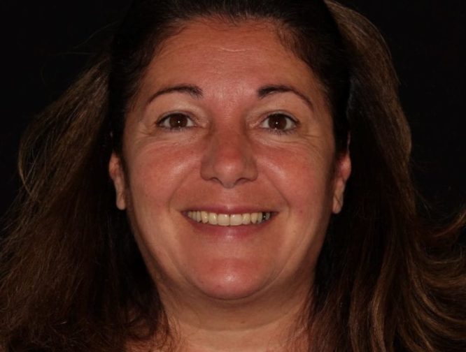 A close-up portrait of a smiling woman with long, wavy brown hair and a black background. she has a joyful expression and visible dimples.