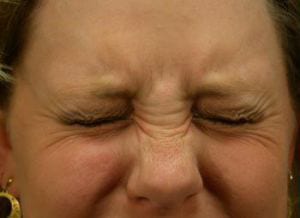 Close-up of a woman's face, eyes tightly closed and eyebrows furrowed, expressing a strong emotion such as frustration or effort.