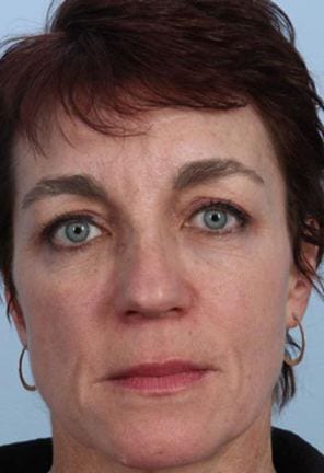 Close-up portrait of a middle-aged woman with short brown hair and striking green eyes, looking directly at the camera, against a plain background.