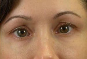 Close-up view of a woman's face focused on her eyes, showing brown eyes, light skin, and arched eyebrows, with a neutral expression.