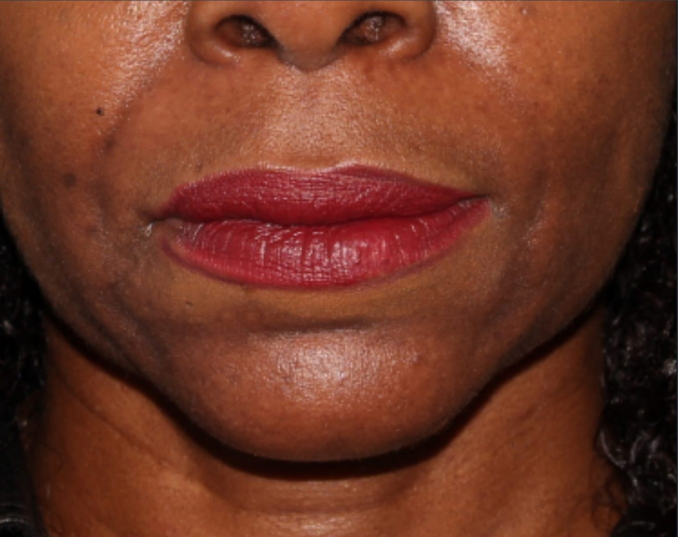 Close-up image of a woman's lips painted with red lipstick, showcasing her full lips and the lower part of her nose. the background is out of focus, emphasizing her facial feature.
