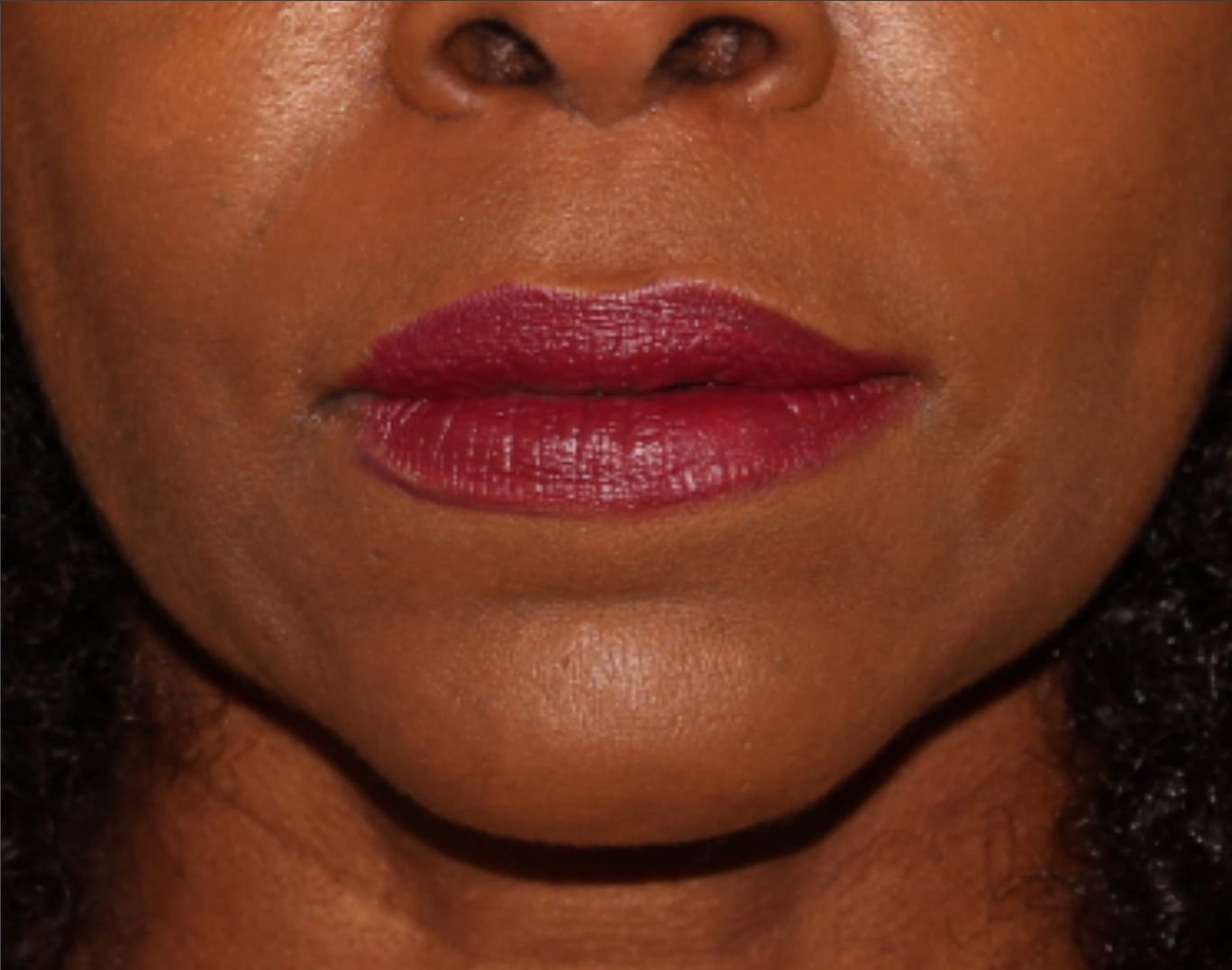 Close-up of a woman's lips painted with red lipstick, focusing on the lower half of her face showing part of her nose and chin. her skin is smooth with a natural glow.