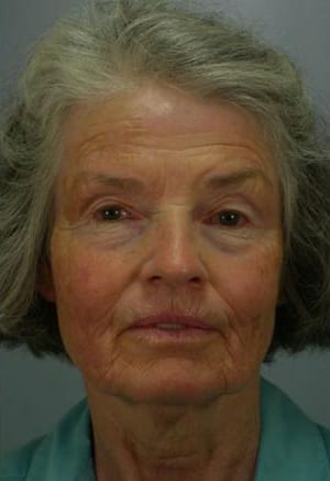 Portrait of an elderly woman with gray hair and a subtle smile, wearing a light blue shirt against a grey background.