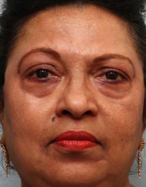 Close-up portrait of a woman with a serious expression, wearing red lipstick and gold earrings, looking directly at the camera.