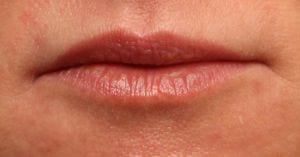 Close-up of a person's lips showing natural pink color with a slight gloss finish, set against a neutral skin tone background.