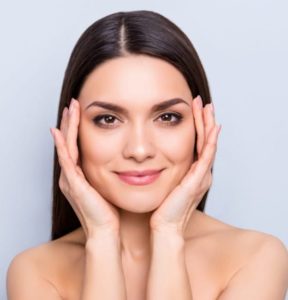 closeup of a woman with her hands on her face smiling with minimal makeup on