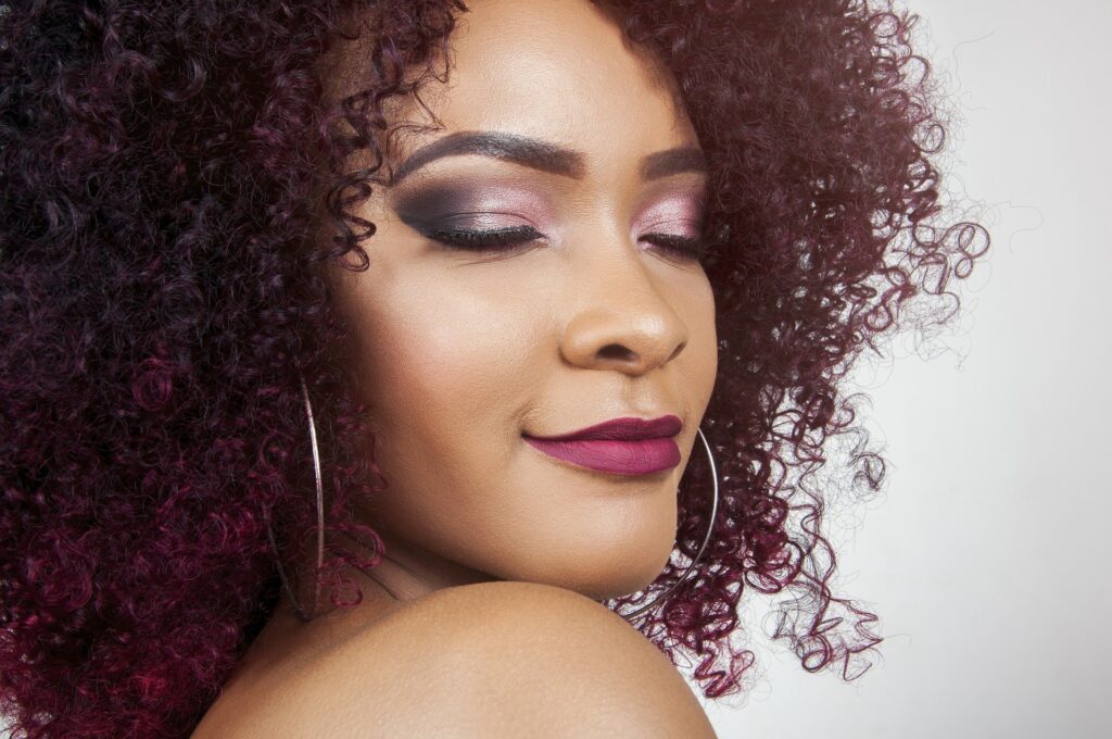 woman with brown and purple curly hair with full, pouty lips wearing deep red lipstick
