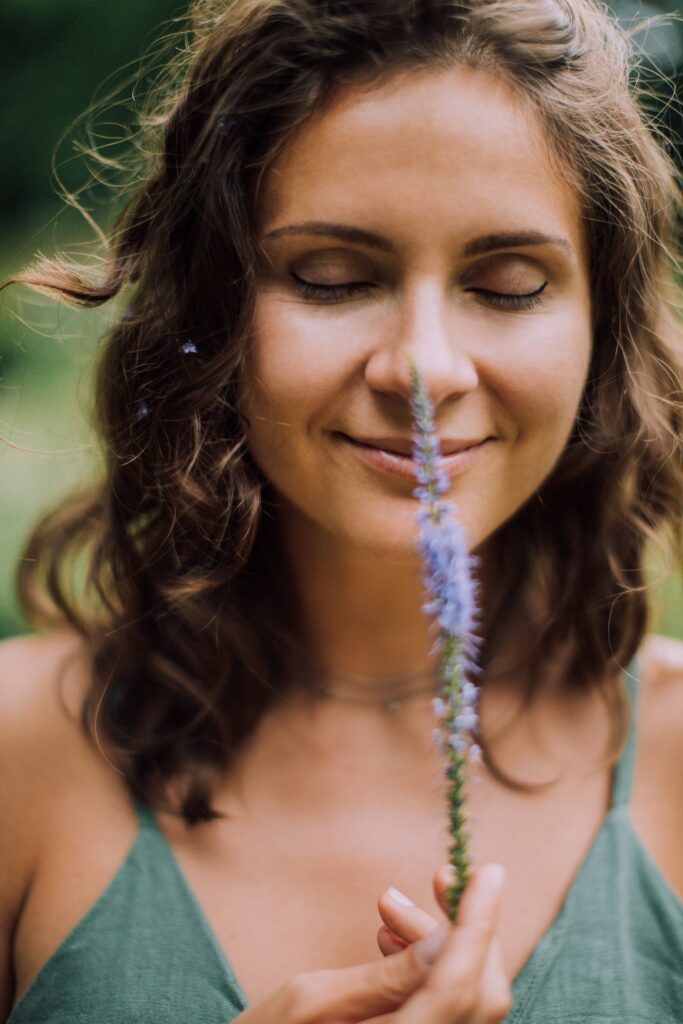 woman with closed eyes tickling her nose with a flower