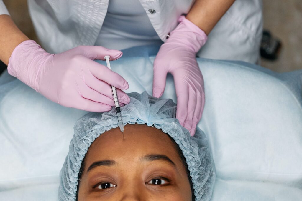 person wearing pink latex gloves holding a medical needle injecting Botox® into the forehead of an adult woman