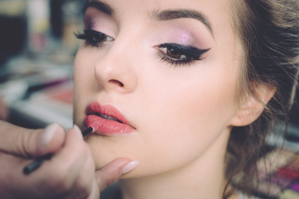 woman with brown hair wearing pink eyeshadow and black winged eyeliner having pink lipstick applied to her lips