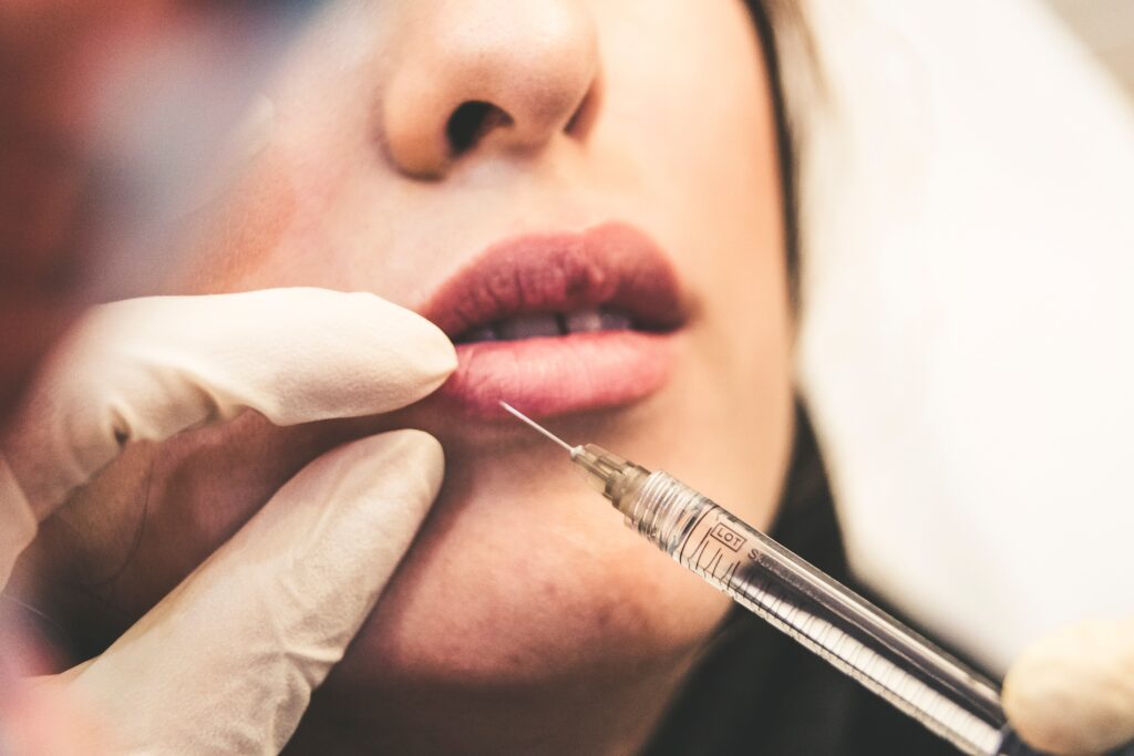 hands wearing latex gloves using a medial needle to inject Botox® into a woman’s pink lips