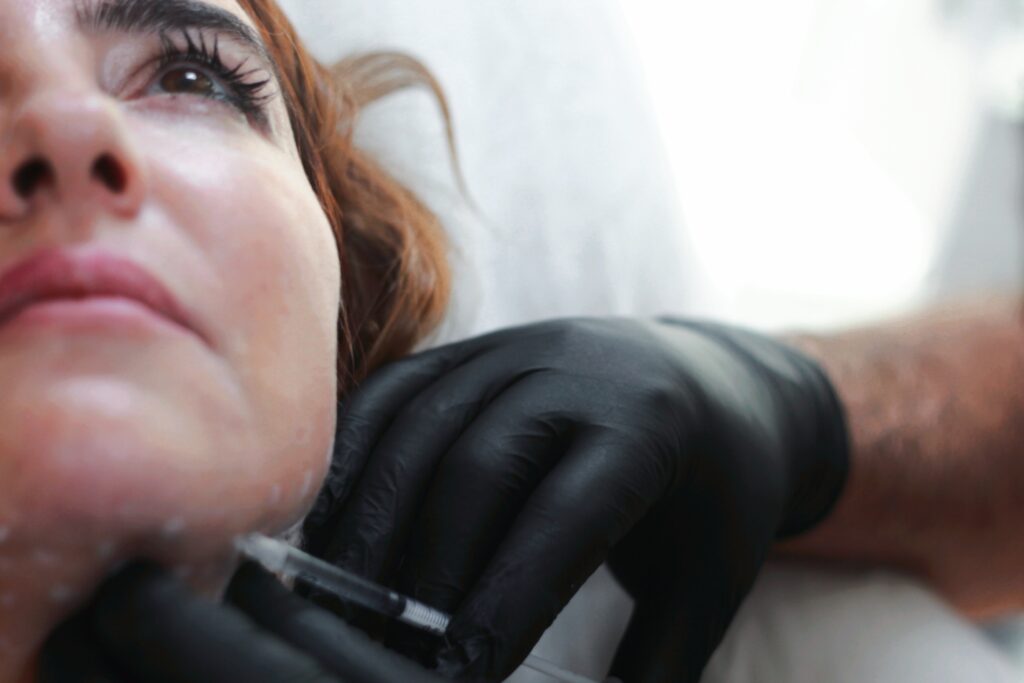 medical professional wearing black latex gloves injecting Botox into the jawline of a woman with brown hair