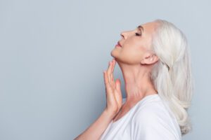 adult woman with white and gray hair touching her chin after receiving a non-surgical neck lift