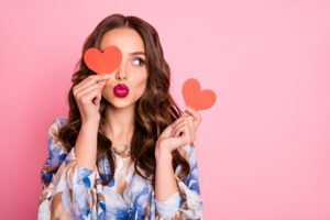 Woman holding heart cutouts with red lipstick and flower shirt
