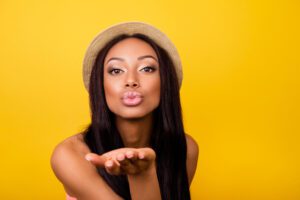 woman wearing straw hat blowing a kiss with a yellow background