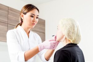 Young woman doctor beautician in white lab coat and sterile gloves draws a marking on woman's cheekbones before injecting Botox to correct forms