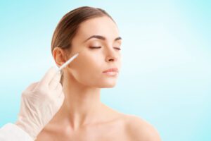 Portrait of an attractive young woman receiving botox treatment. Isolated on light blue background.