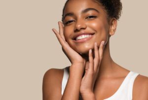 young woman smiling with hand on her face, with clear, beautiful skin